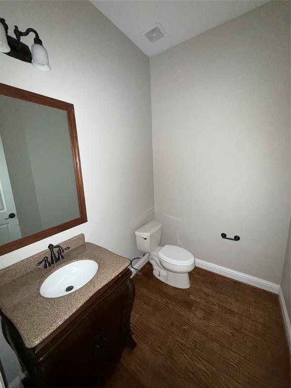 Bathroom featuring a wood-finish vanity, solid surface countertop with an integrated basin, wood-finish flooring, and a wall-mounted vanity mirror with a decorative frame