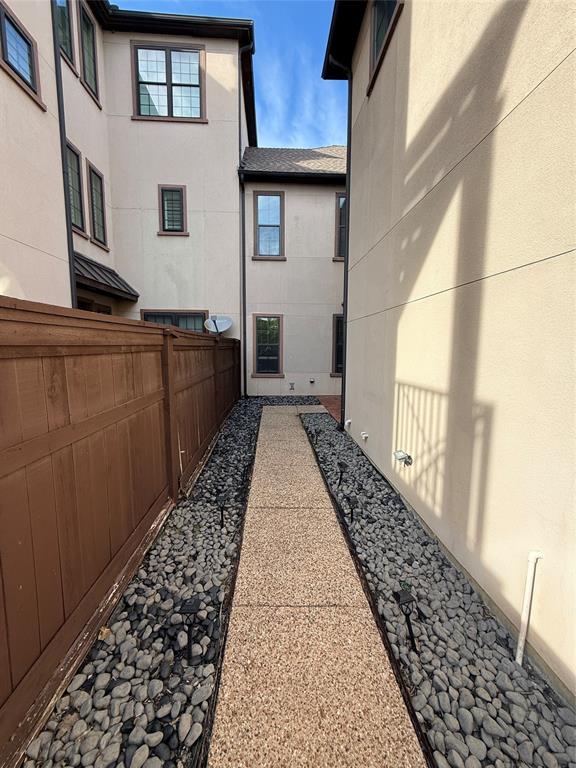 Exterior side path featuring a textured aggregate walkway, decorative stone border, integrated landscape lighting, and a solid wood privacy fence Exterior side path featuring a textured aggregate walkway, decorative stone border, integrated landscape lighting, and a solid wood privacy fence