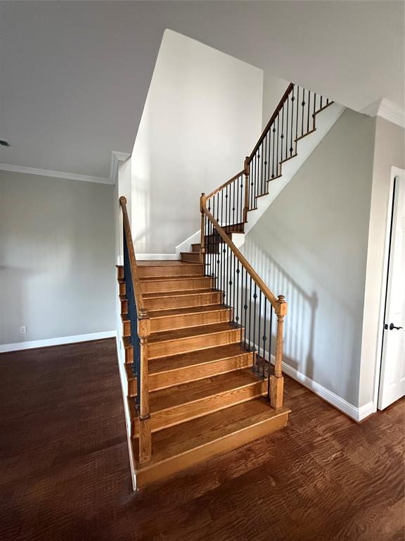 Staircase featuring wood-finish treads, square newel posts, and decorative metal balusters set against wood-finish flooring Staircase featuring wood-finish treads, square newel posts, and decorative metal balusters set against wood-finish flooring