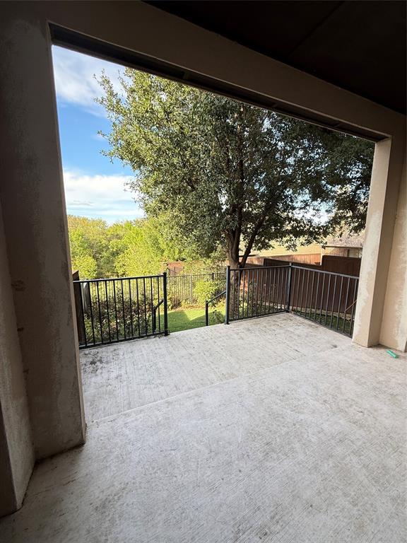 Covered concrete patio featuring a black metal railing and a backdrop of mature trees Covered concrete patio featuring a black metal railing and a backdrop of mature trees