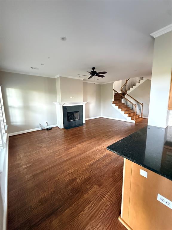 Living area featuring wood-finish flooring, a fireplace with a dark stone surround, a central ceiling fan, and a staircase with wood treads and decorative metal balusters Living area featuring wood-finish flooring, a fireplace with a dark stone surround, a central ceiling fan, and a staircase with wood treads and decorative metal balusters