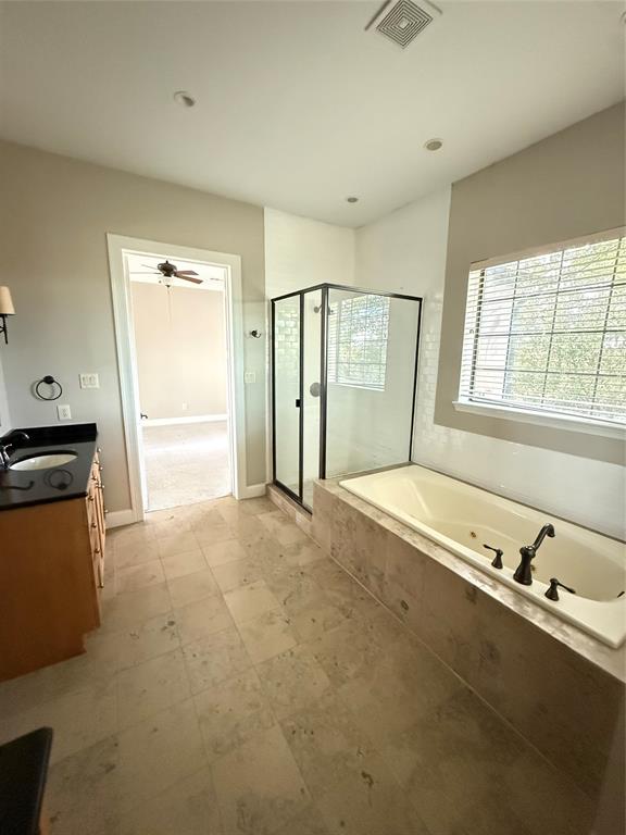 Bathroom featuring a soaking tub with tile surround, glass-enclosed shower with matte black frame, dark stone countertop, wood-finish cabinetry, and large-format tile flooring
