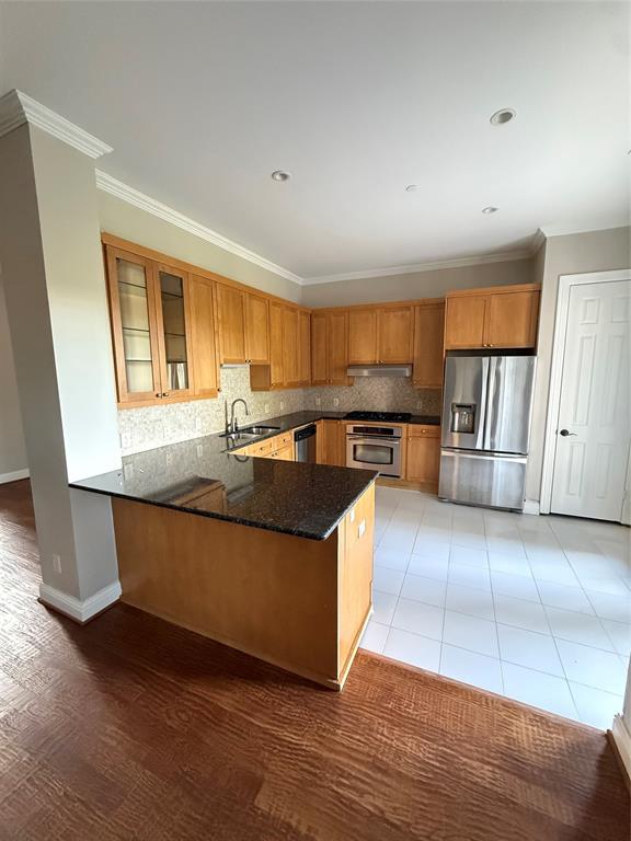 Kitchen featuring wood cabinetry, stone countertops, stainless steel appliances, a peninsula, and tile flooring Kitchen featuring wood cabinetry, stone countertops, stainless steel appliances, a peninsula, and tile flooring
