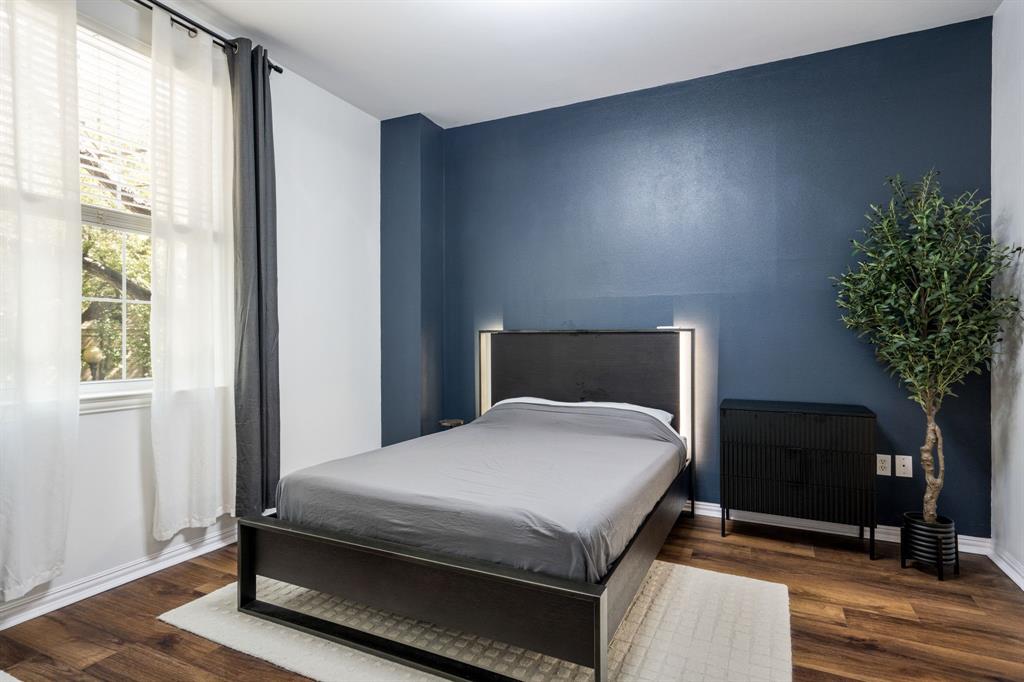 Bedroom featuring a deep blue accent wall, wood-finish flooring, and a large window with natural lighting