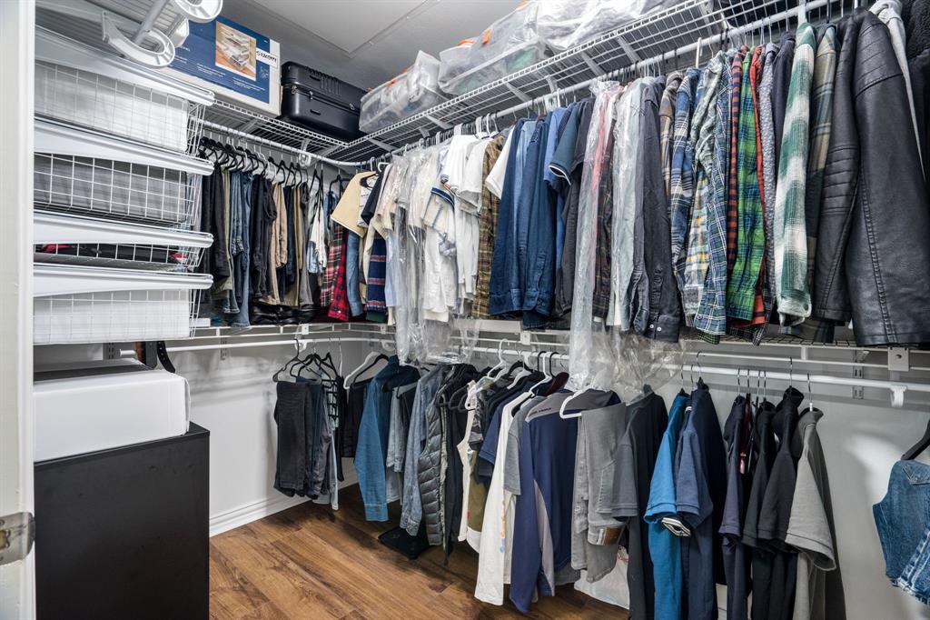 Walk-in storage area featuring multi-tiered white wire shelving, overhead storage racks, and wood-finish flooring