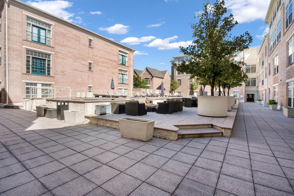 Paved courtyard terrace featuring brick building exteriors, tiered stone-finished hardscaping, and integrated concrete planters with mature trees