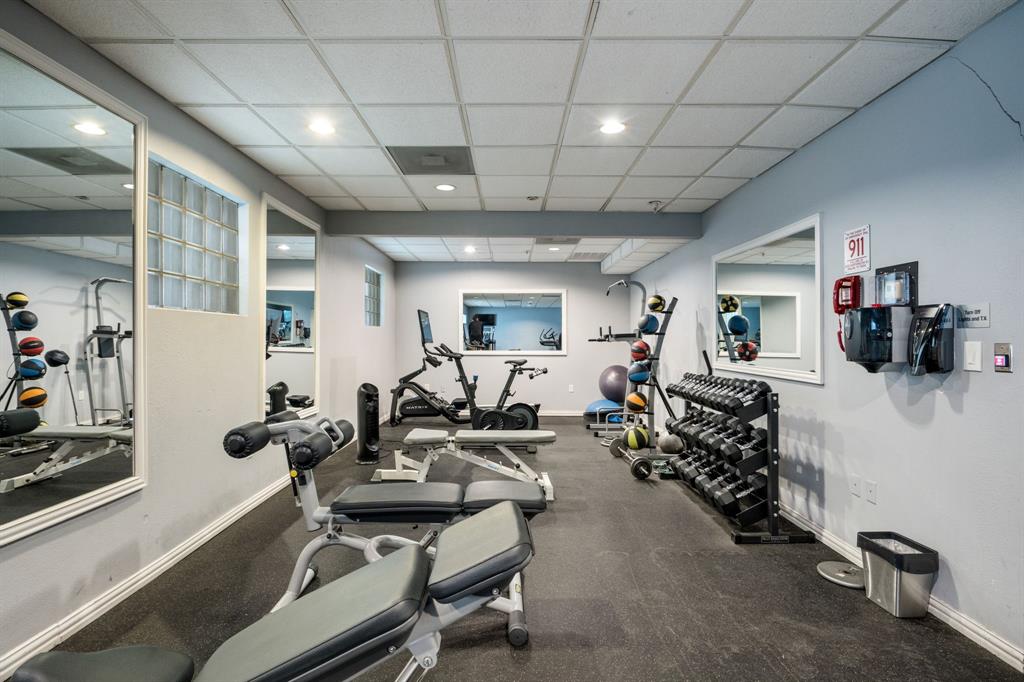Fitness area featuring wall-to-wall mirrors, recessed lighting, drop ceiling, glass block accent windows, and rubberized flooring