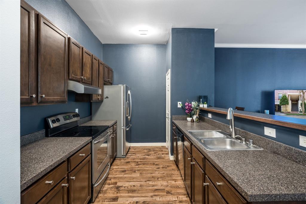 Kitchen featuring dark wood cabinetry, textured countertops, stainless steel appliances, a dual-basin stainless steel sink with a high-arch faucet, and wood-finish flooring