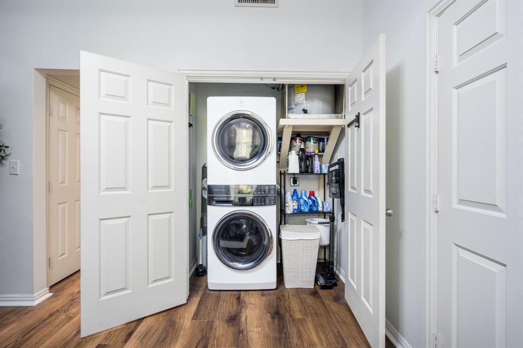 Laundry closet featuring stackable washer and dryer, wood-finish flooring, and recessed storage shelving