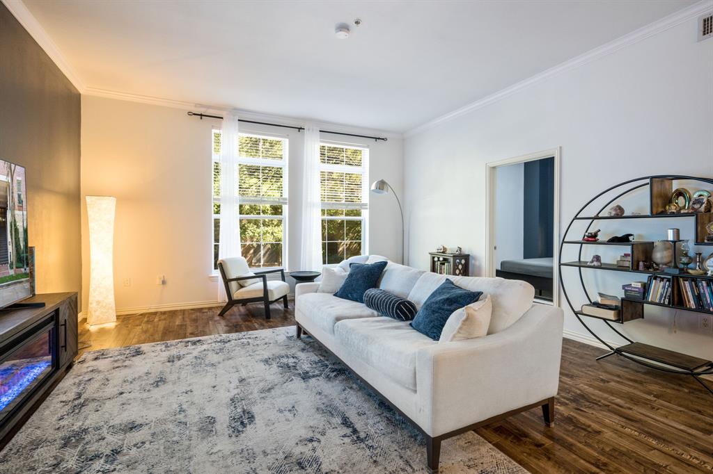 Living area featuring wood-finish flooring, high ceilings with crown molding, and tall windows