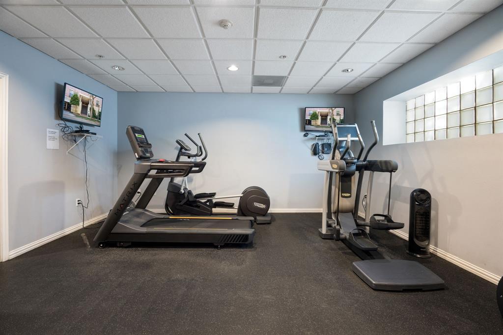 Fitness area featuring textured rubber flooring, a drop-tile ceiling with recessed lighting, and a glass block window