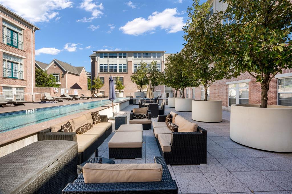 Outdoor pool with tile surround, paved terrace, and oversized cylindrical concrete planters featuring mature trees