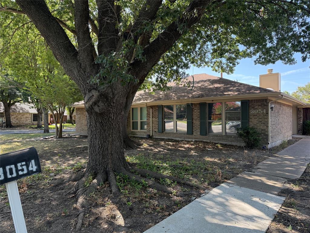 Single-story brick exterior featuring a hip roof, chimney, shutter-framed windows, and mature trees Single-story brick exterior featuring a hip roof, chimney, shutter-framed windows, and mature trees