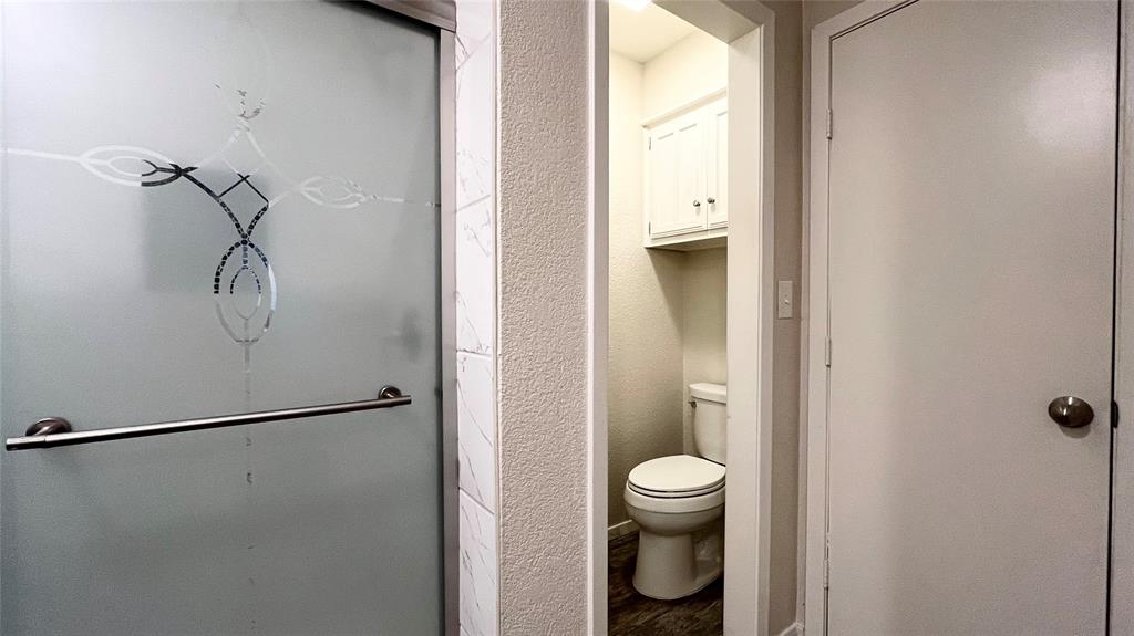 Frosted glass shower door with metallic handle, neutral wall tile, two-piece toilet, and built-in upper wall cabinetry
