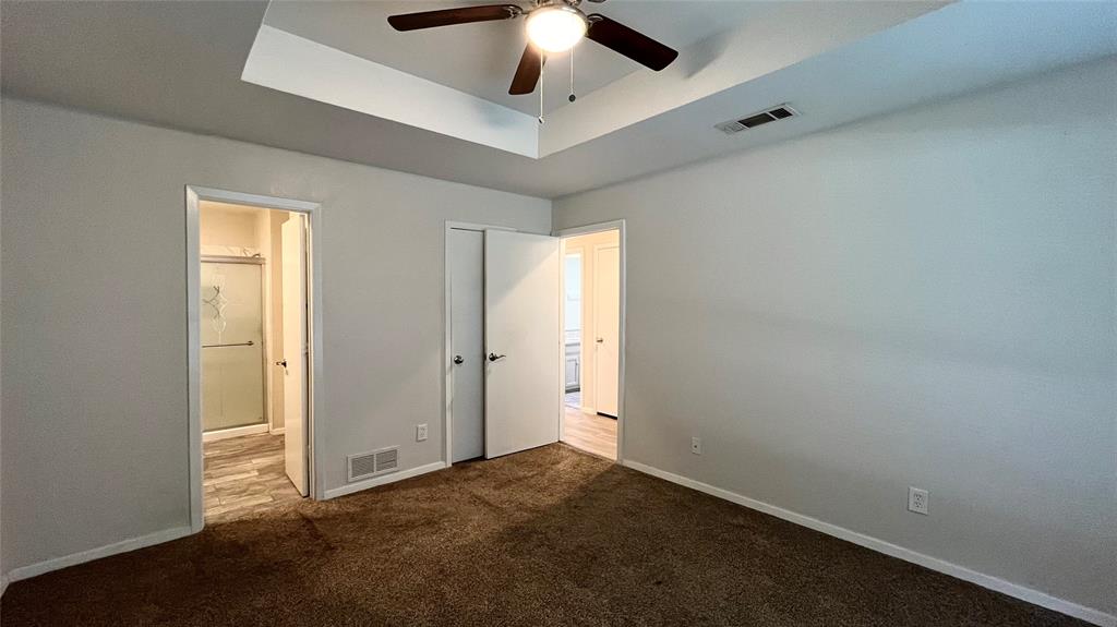 Tray ceiling featuring a central ceiling fan with integrated lighting, neutral wall finishes, and carpeted flooring