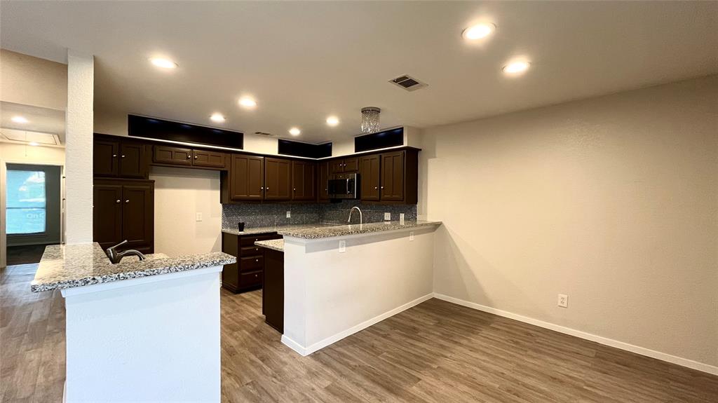 Kitchen featuring dark cabinetry, stone-surface countertops, wood-finish flooring, recessed lighting, and a breakfast bar Kitchen featuring dark cabinetry, stone-surface countertops, wood-finish flooring, recessed lighting, and a breakfast bar