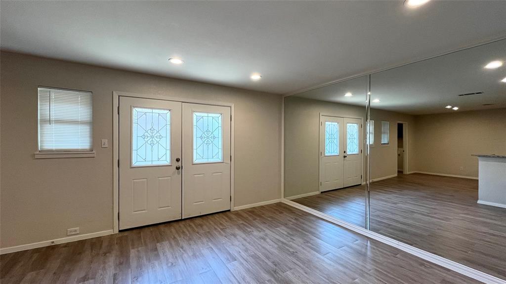 Double entry doors with decorative glass inserts, recessed lighting, wood-finish flooring, and a floor-to-ceiling mirrored wall Double entry doors with decorative glass inserts, recessed lighting, wood-finish flooring, and a floor-to-ceiling mirrored wall