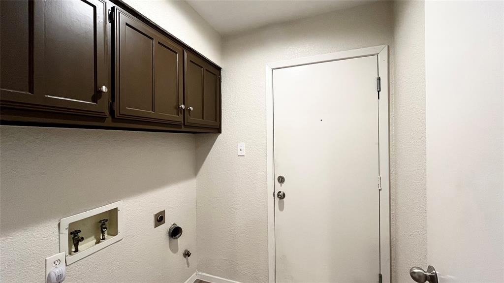 Utility area featuring dark-finish upper cabinetry, integrated plumbing hookups, and a solid-core entry door with dual locking mechanisms Utility area featuring dark-finish upper cabinetry, integrated plumbing hookups, and a solid-core entry door with dual locking mechanisms