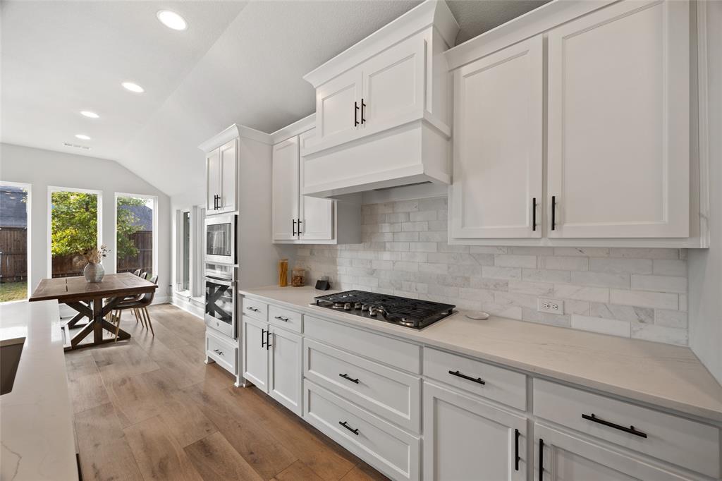 Kitchen featuring white shaker-style cabinetry, a stone-tiled backsplash, integrated gas cooktop, built-in double oven, and wood-finish flooring