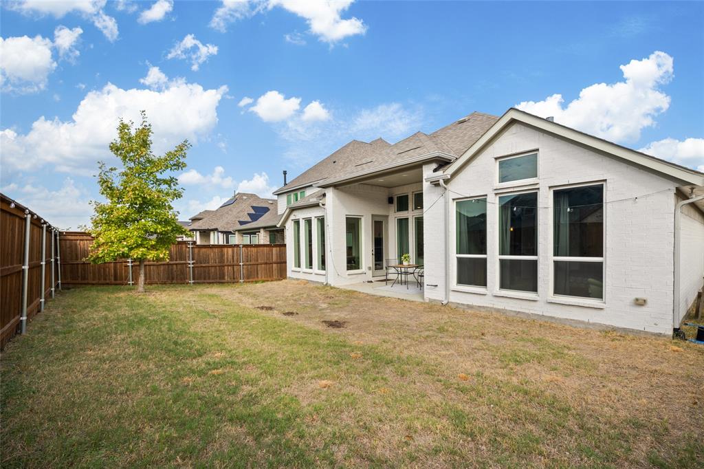 Rear exterior featuring a white-painted brick facade, covered patio, multiple tall windows, and a wood privacy fence enclosing the backyard