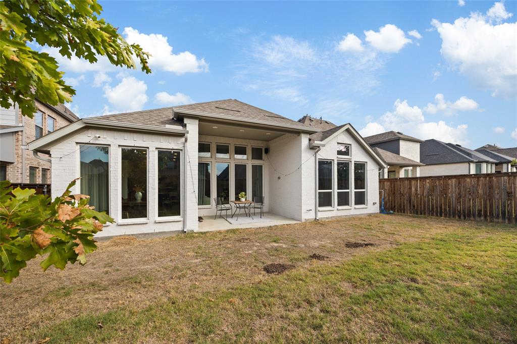 Painted brick exterior featuring a covered patio, expansive windows with grid detailing, and a fenced backyard