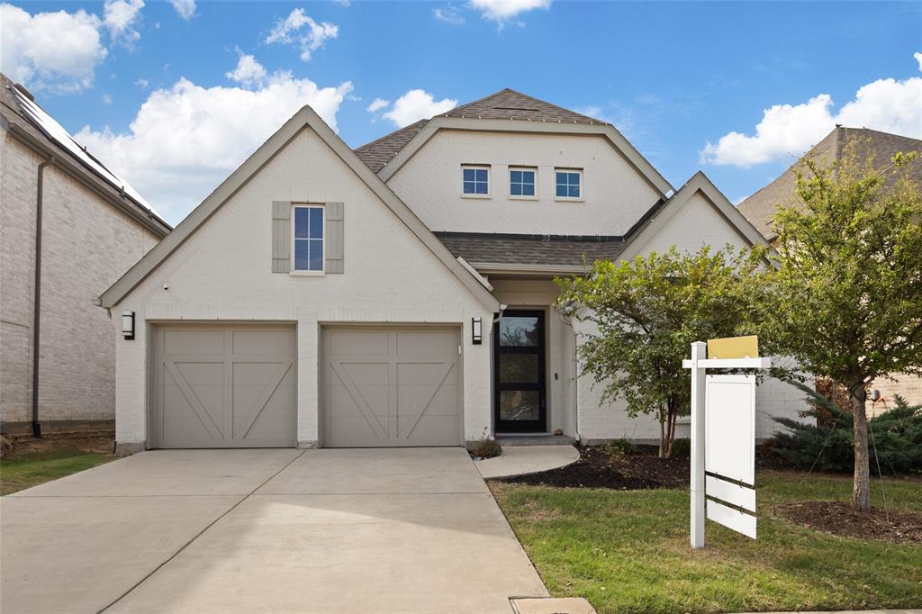 Light-colored brick exterior with a multi-gable roofline, two-car garage with carriage-style doors, and contemporary glass-panel front entry door