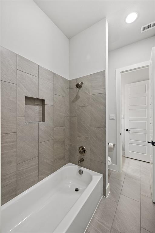Bathtub with ceramic tile surround, integrated recessed shelving, and metallic shower fixtures, complemented by large-format floor tiling and a five-panel interior door