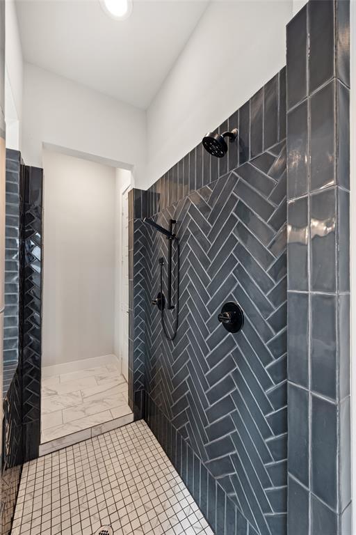 Walk-in shower featuring charcoal-toned subway tile arranged in a herringbone pattern, matte black wall-mounted shower fixtures, handheld sprayer, and stone-look floor tiling