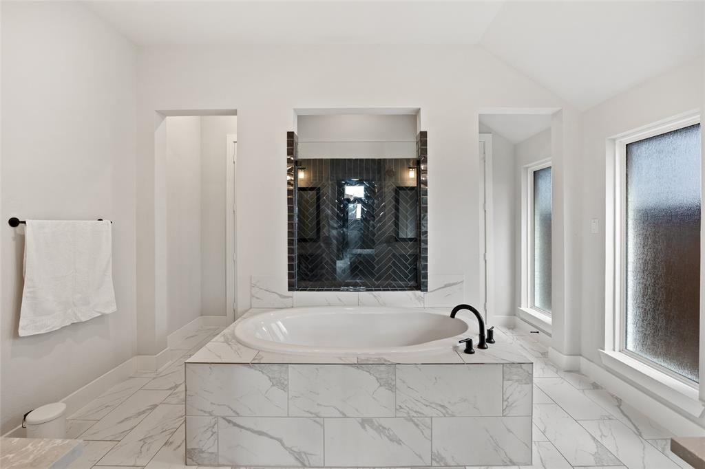 Built-in soaking tub with a tiled surround, herringbone-patterned wall accent, matte black plumbing fixtures, and tile flooring