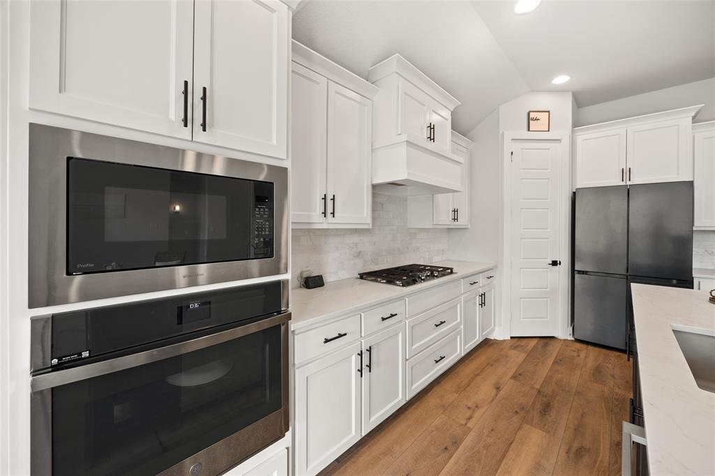 Kitchen featuring white shaker-style cabinetry, stainless steel built-in double ovens and microwave, quartz countertops, gas cooktop, and wood-finish flooring