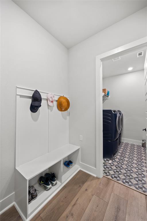 Built-in white mudroom bench featuring integrated shelving and wall-mounted coat hooks, wood-finish flooring, and patterned tile flooring
