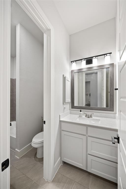 White cabinetry with a solid-surface countertop, rectangular undermount sink, framed mirror, and multi-light vanity fixture, featuring tile flooring