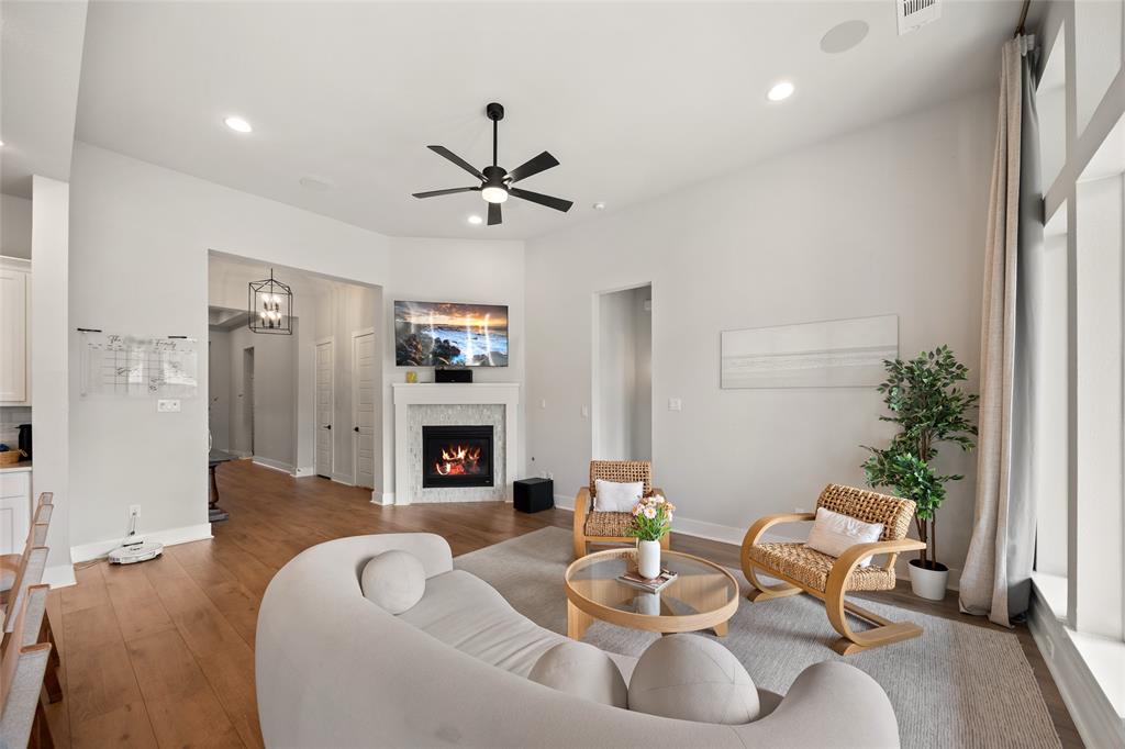 Living area featuring high ceilings, wood-finish flooring, a fireplace with a decorative tile surround, recessed lighting, and a multi-blade ceiling fan Living area featuring high ceilings, wood-finish flooring, a fireplace with a decorative tile surround, recessed lighting, and a multi-blade ceiling fan