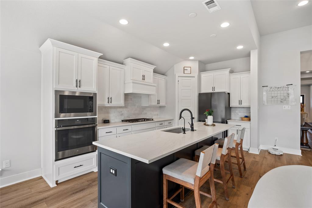 Kitchen featuring white shaker-style cabinetry, an expansive center island with a stone countertop, recessed lighting, stainless steel built-in double ovens, and wood-finish flooring