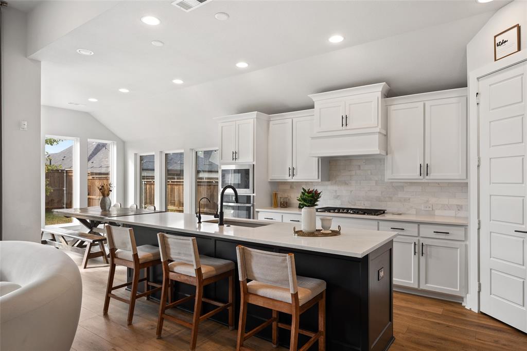 Kitchen featuring white shaker-style cabinetry, dark contrast kitchen island with a light-toned countertop, subway tile backsplash, built-in double oven, and wood-finish flooring