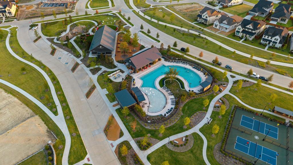 Community amenities featuring an expansive swimming pool, zero-entry splash area, multiple covered pavilion structures, and dual hard-court athletic surfaces situated within landscaped grounds