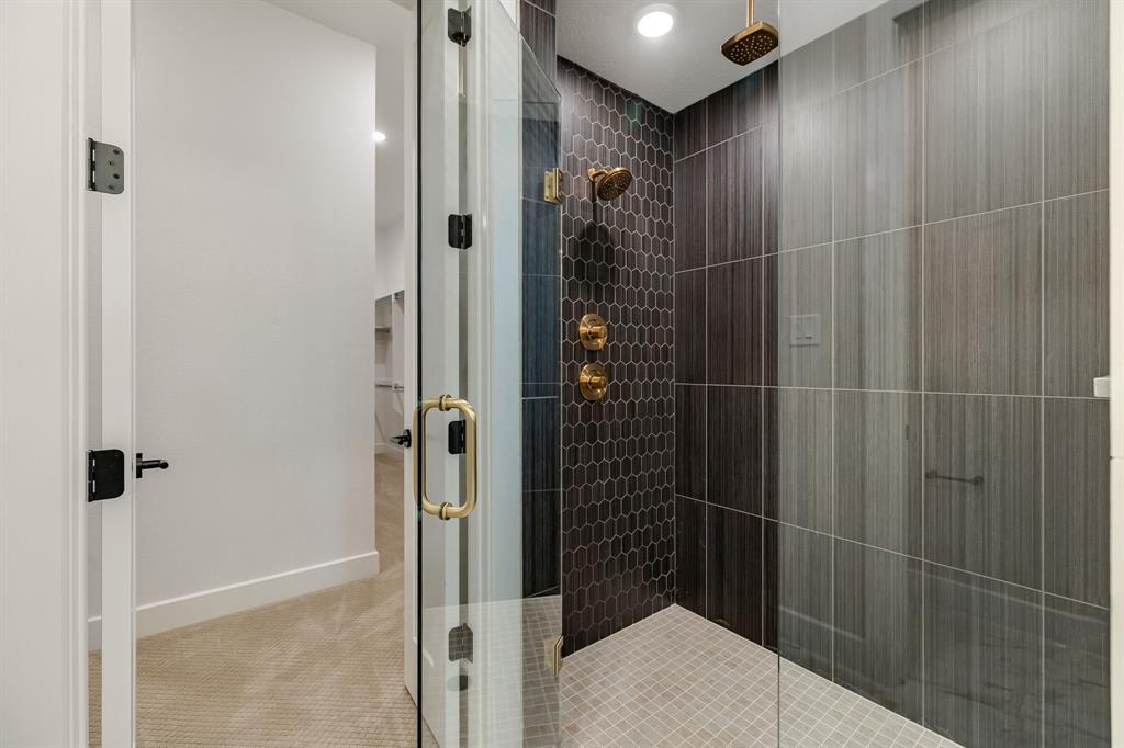Walk-in shower featuring a glass enclosure, brass-finish rainfall showerhead and wall-mounted controls, hexagonal dark-toned accent tile, and large-format gray wall tile