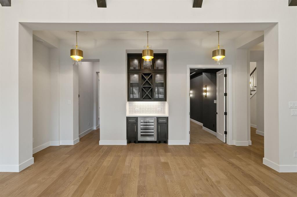 Built-in wet bar featuring dark cabinetry, integrated wine refrigerator, glass-front upper storage, tile backsplash, and trio of pendant light fixtures over wood-finish flooring