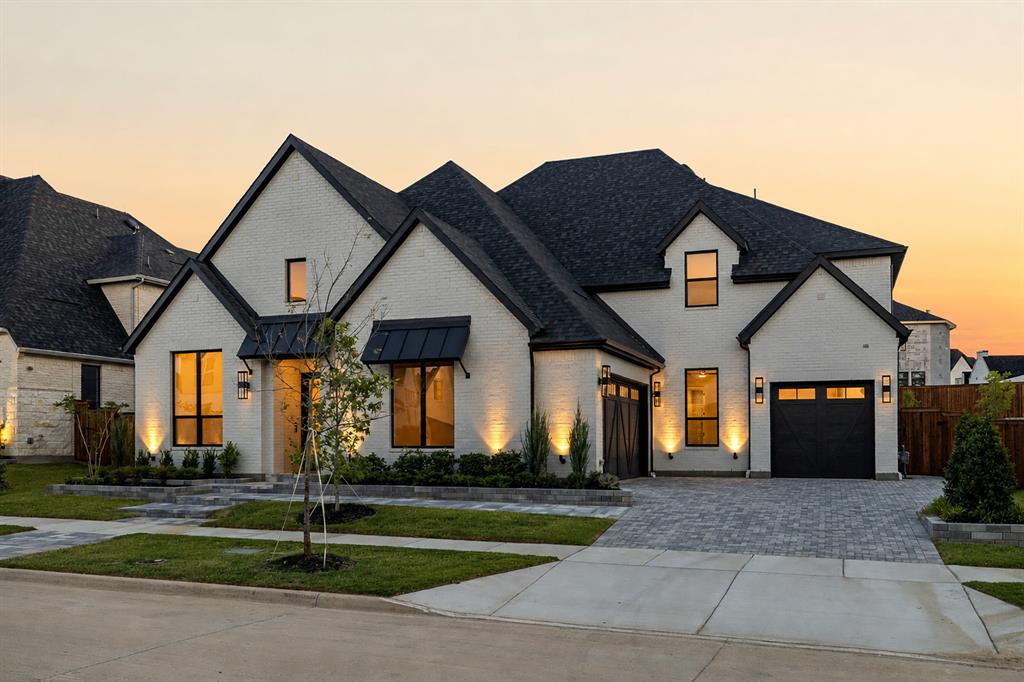 Multi-gabled exterior featuring light masonry, dark shingle roofing, black metal awnings, and an expansive paved driveway