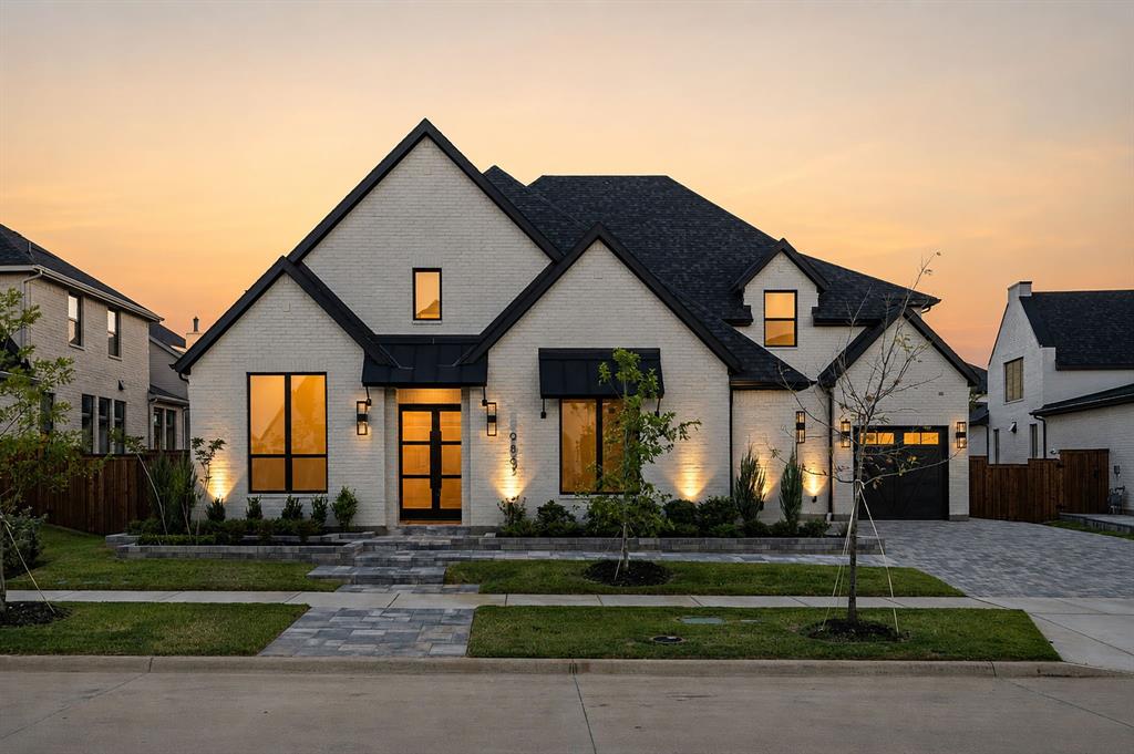Traditional brick exterior featuring a multi-gabled roofline, dark metal window awnings, a paved stone driveway, and a modern multi-lite glass front door