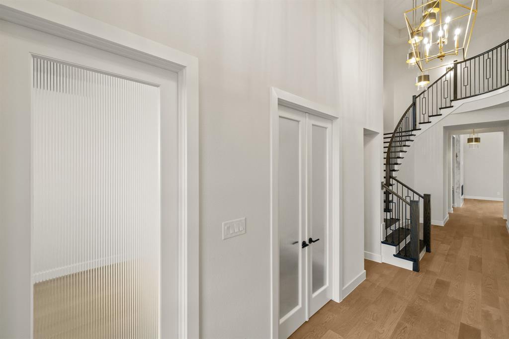 Curved staircase with metal railing, fluted glass-panel doors, high ceilings, wood-finish flooring, and multi-tier geometric chandelier