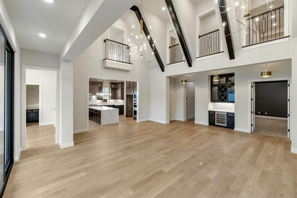 Vaulted ceilings featuring exposed timber beams, wood-finish flooring, a built-in wet bar with wine refrigeration, multi-level balcony railings, and recessed lighting