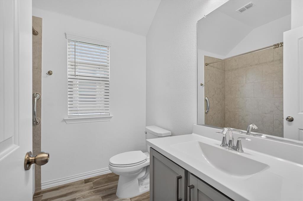 Bathroom featuring a grey vanity with a white countertop, an integrated basin, wood-finish flooring, and a tiled shower enclosure with metal grab bars