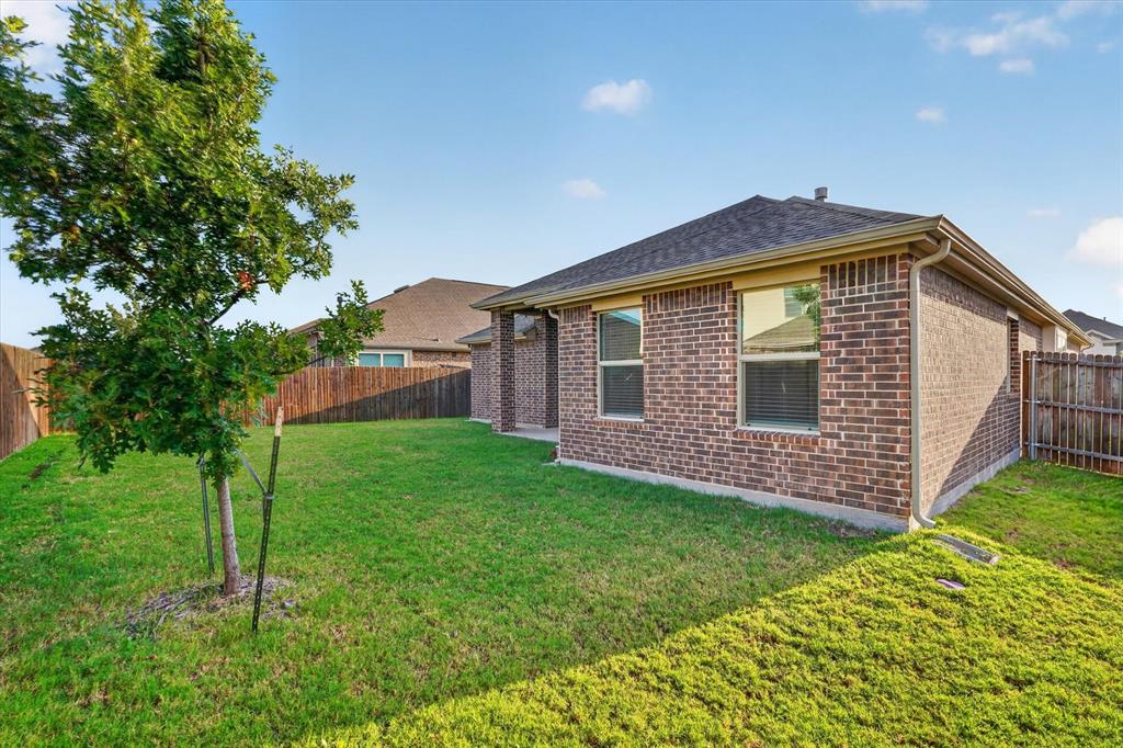 Brick exterior featuring a hip roof, covered patio, grass lawn, and wood privacy fencing