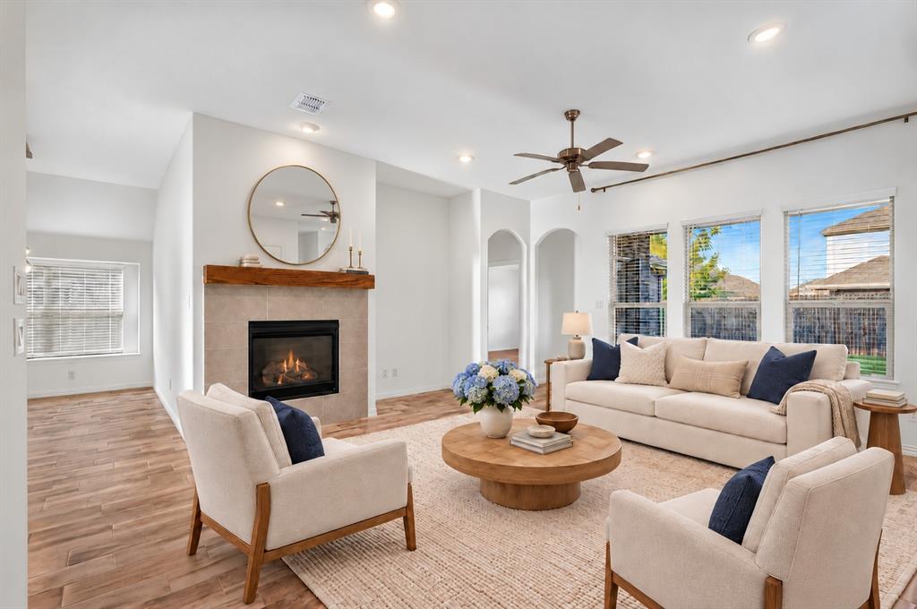 Living area featuring wood-finish flooring, a fireplace with a stone-tile surround and timber mantel, recessed lighting, and a multi-blade ceiling fan Living area featuring wood-finish flooring, a fireplace with a stone-tile surround and timber mantel, recessed lighting, and a multi-blade ceiling fan