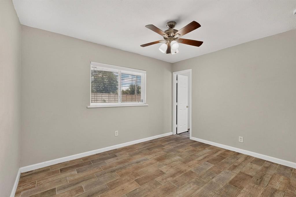 Spacious primary bedroom showcasing a ceiling fan, a wide window, hardwood floors and an en suite bath, inviting comfort and style.