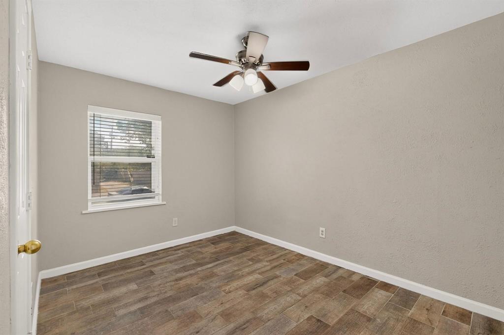 A well-lit third bedroom with a ceiling fan and a window providing a view outside.