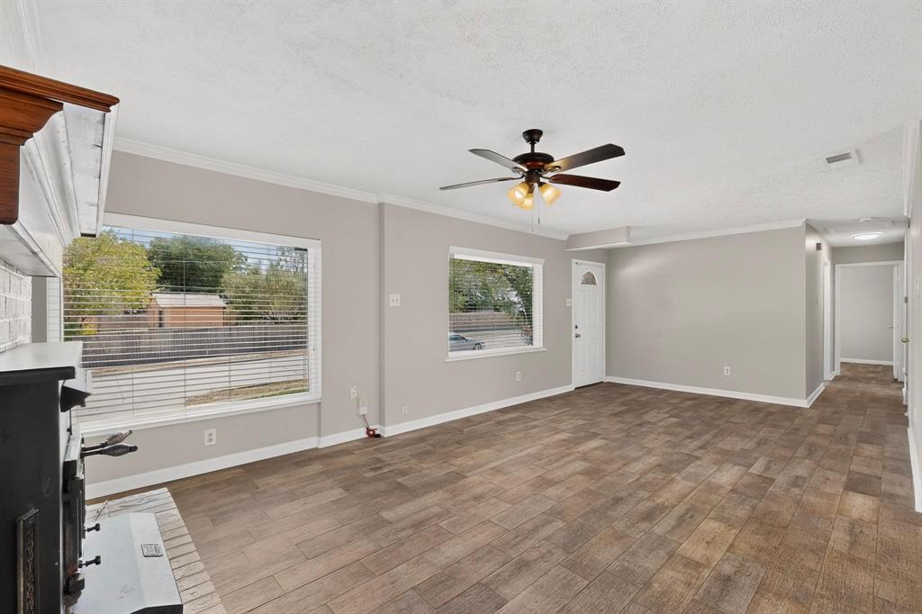A bright living room featuring hardwood floors, a fireplace, a ceiling fan and wide windows, creating a spacious and airy atmosphere. A bright living room featuring hardwood floors, a fireplace, a ceiling fan and wide windows, creating a spacious and airy atmosphere.