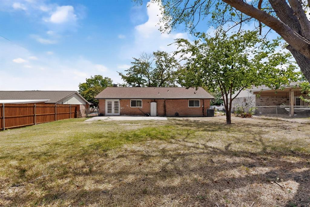 A grassy yard with a patio and a lush tree enclosed by a wooden fence, inviting a sense of tranquility.