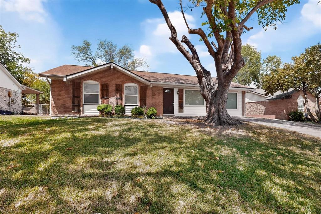 A charming brick home set in a large yard, featuring a green yard and a large tree for shade and beauty.